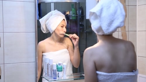 Woman Brushing Her Teeth in Bathroom Mirror