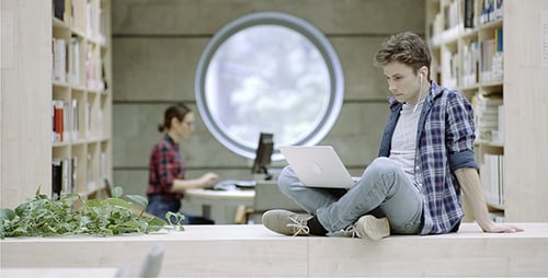 Young Man Works on Laptop in Library Setting