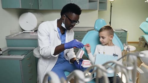 Dentist Showing Young Boy How To Brush Teeth