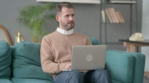 Man with Laptop Thinking on Sofa