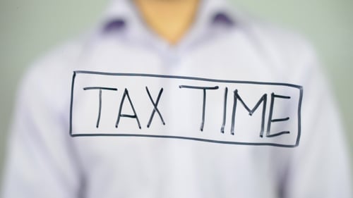 Adult Hand Writing Tax Time on Clear Surface