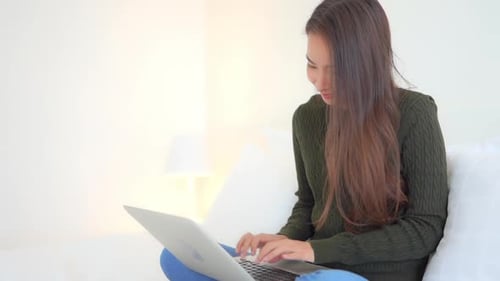 Woman Works on Laptop Computer While Sitting on Bed