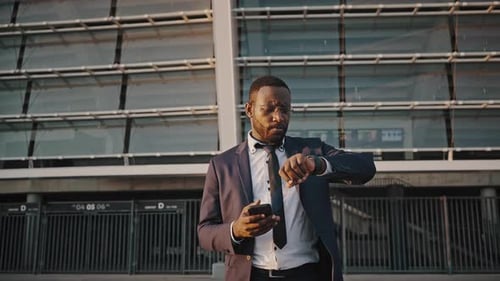 Stylish Businessman Checks Time on Mobile Device and Watch