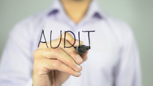 Man Writes the Word Audit on Clear Surface