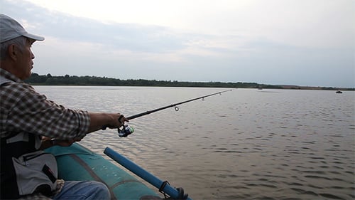 Man Fishing on Lake with Fishing Rod and Boat