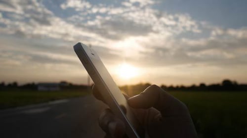 Hand Holding Smartphone at Sunset in Rural Area