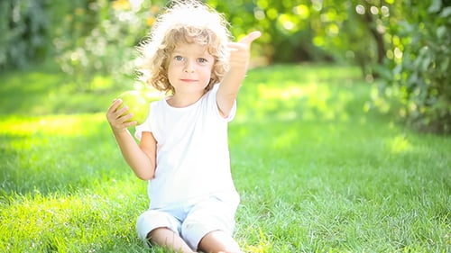 Happy Child Playing with Apple on Grass