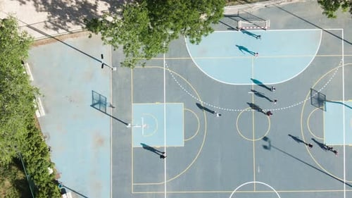 Locals playing basketball in blue outdoor court on hot daylight, top down aerial