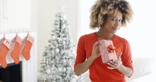 Woman Holding Christmas Gift near Tree in Home