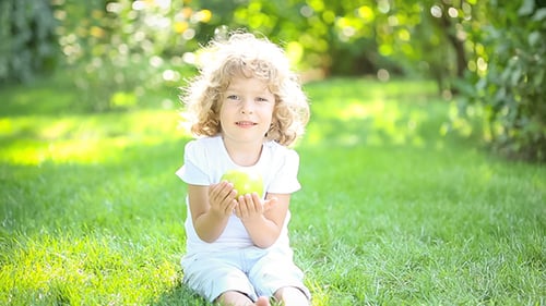 Happy Child Eating Apple Outdoors in Summer