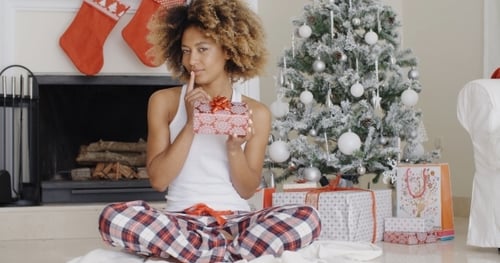 Woman Holding Gift in Front of Christmas Tree