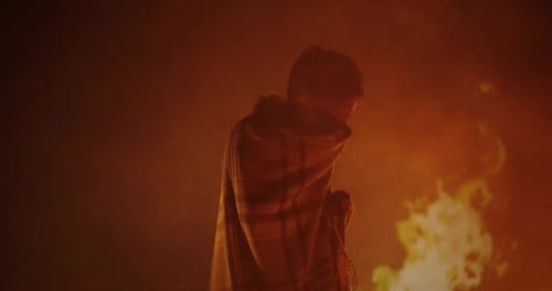 Teen Wrapped in Shawl Stands Before Fiery Blaze