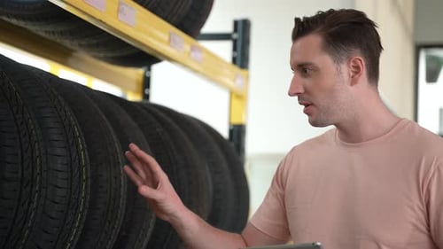 technician service person working in garage car to recommend and sell a tire on shelf storage