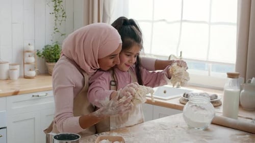 MiddleEastern Mom And Daughter Kneading Dough Together Baking In Kitchen