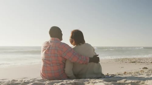 Smiling senior african american couple embracing and sitting on sunny beach