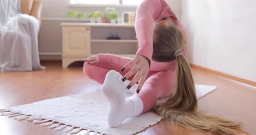 Close-up of woman in pink sportswear practicing forward bends doing yoga at home in apartment