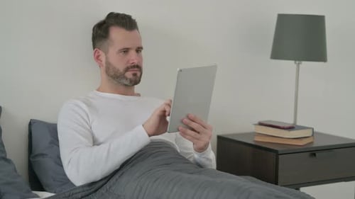 Man Using Tablet in Bed, Frustrated with Technology