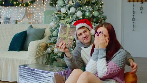 Paar sitzt auf dem Boden in der Nähe des Weihnachtsbaums im Wohnzimmer