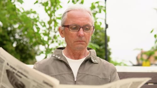 Senior Man in Glasses Reading Newspaper in the Park