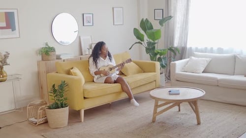 Woman Plays Ukulele on Yellow Couch in Living Room