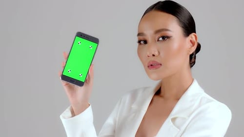 Beautiful Asian businesswoman showing smartphone with green screen