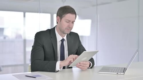 Hardworking Middle Aged Businessman Using Tablet in Office