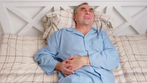 Man in Bed Holding Stomach in Pain