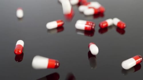 Rote Arzneimittelkapseln und Pillen mit verschreibungspflichtigen Medikamenten fallen in Zeitlupe auf einem schwarzen isolierten Hintergrund