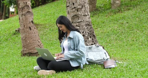Seitenansicht einer Frau, die im Park sitzt und Laptop benutzt