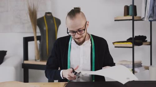 Young Designer or Tailor Sitting at a Working Sewing Table at the Studio