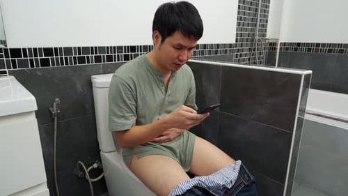 man with stomachache talking on a mobile phone and sitting in toilet bowl in the bathroom at home
