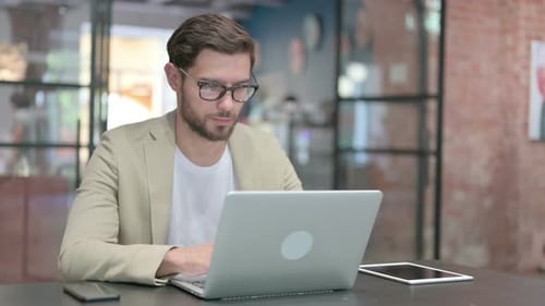 Young Adult Typing on Laptop in Office Setting