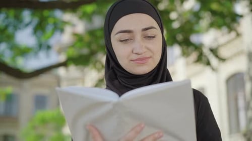 Close-up of Concentrated Muslim Woman Reading Book Outdoors. Absorbed Young Beautiful Lady Enjoying