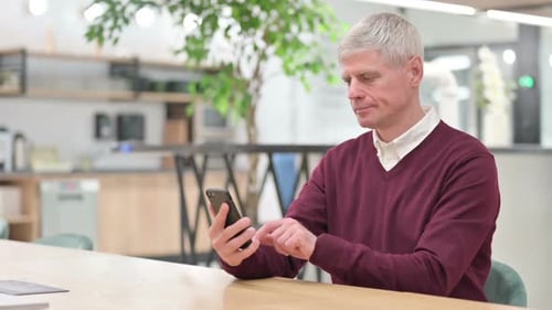 Mann mittleren Alters mit Laptop mit Smartphone