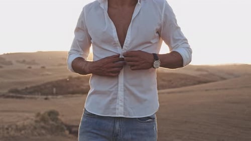 Homem desabotoando camisa no meio do campo de trigo e céu ensolarado no fundo