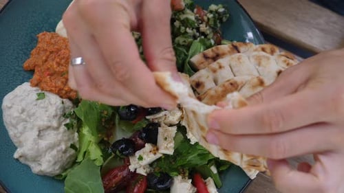 Hands Dipping Pita Bread into Salad and Dips
