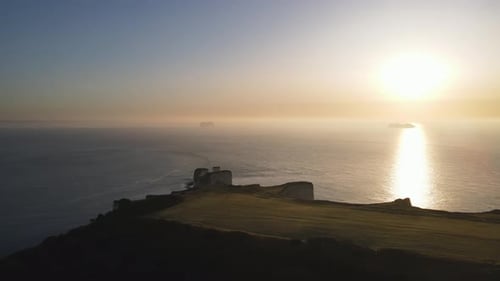 Sun reflecting over sea surface at sunset and ship in background, Old Harry Rocks cliffs. Aerial for