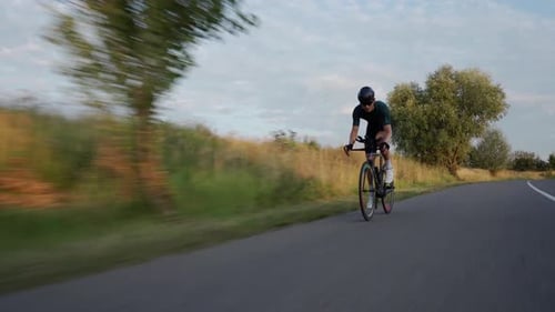 Young fit man cycling on road downhill at sunset