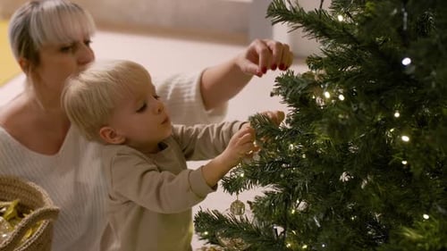 Child Decorates Christmas Tree with Adult Assistance