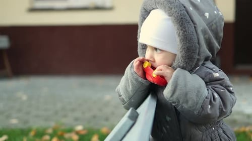 Little Baby Infant in Grey Hood Jumpsuit and White Hat Playing Red Car Outdoors