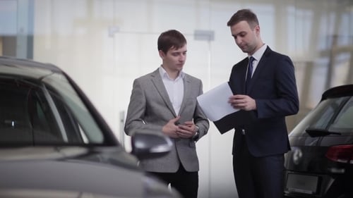 Men Review Paperwork at Car Dealership