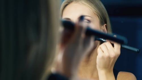 Glamorous Woman Applying Makeup with Brushes in Mirror