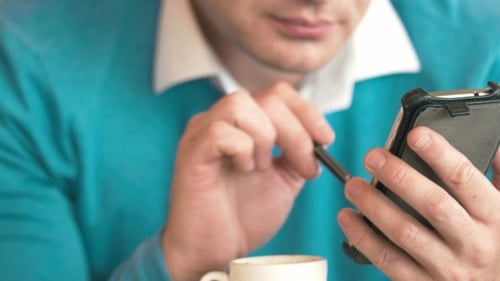 Man Using Cell Phone And Making Notes