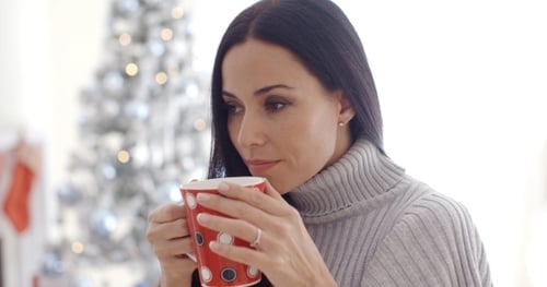 Woman Drinks from Mug by Christmas Tree Indoors
