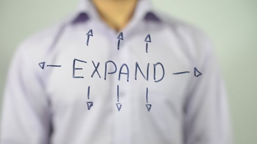 Person Writes 'Expand' with Arrows on Glass