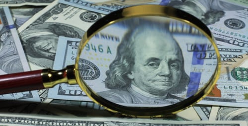 Magnifying Glass Glides Over Pile of US Dollars