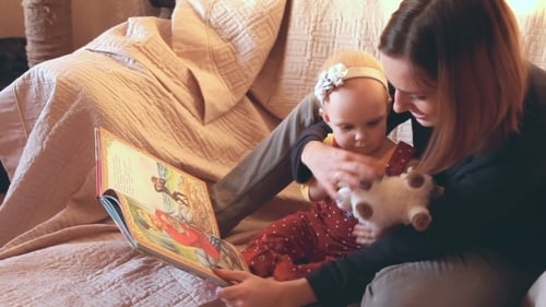 Woman Reads Book to Baby on Sofa