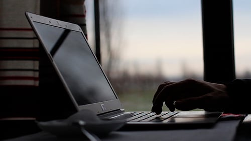Person Typing on Laptop with Coffee by Window