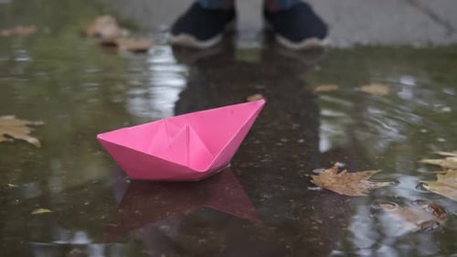 Child Playing with Pink Paper Boat in Puddle
