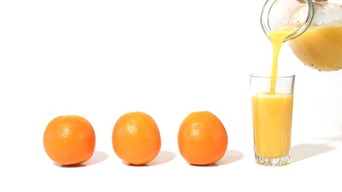 Orange Juice Being Poured into Glass with Oranges